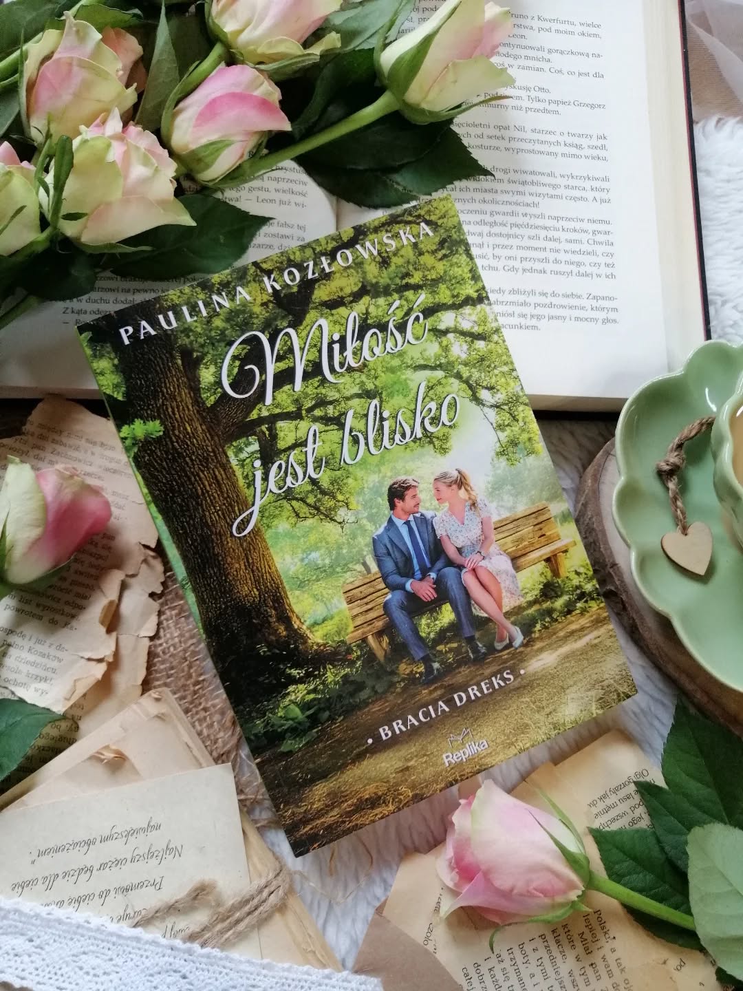 Dzień dobry 🤗  Książka idealna na chwilę relaksu!  “Celem jest zestarzeć się ze wspomnieniami, a nie umrzeć z marzeniami”.  “Miłość jest blisko” Paulina Kozłowska  Wojtek Dreks spędza noc z kobietą,  odrzucona i zraniona zaczyna go prześladować. Zaniepokojona rodzina namawia go, by skorzystał z usług agencji ochrony. Mężczyzna nie przypuszcza jednak, że osobą odpowiedzialną za jego bezpieczeństwo okaże się… kobieta – i to sporo niższa od niego. Iga Daniec jest młodą, ambitną profesjonalistką, która wcale nie jest zachwycona przydzielonym zadaniem. Ochrona aroganckiego biznesmena nie brzmi jak coś, o czym marzyła – zwłaszcza teraz, gdy sama zmaga się z własnymi problemami. Ich pierwsze spotkania pełne są napięcia i wzajemnych uszczypliwości. Współpracy nie ułatwia także wyraźnie wyczuwalna między nimi chemia. Co z tego wyniknie?  Lekka, przyjemna opowieść z nutą romansu, szczyptą sensacji, z umiejętnie wplecionymi trudniejszymi tematami. Urzekł mnie jej klimat, ciepły, naturalny, przepełniony dobrym humorem, a jednocześnie pełen emocji.  Iga to kobieta pracująca w branży ochroniarskiej zdecydowanie wyróżnia się na tle innych bohaterek i nadaje tej historii wyjątkowego charakteru.  Relacja bohaterów to czysta energia. Na początku aż iskrzy od uszczypliwości i napięcia, ale z czasem między nimi pojawia się coś więcej. Autorka buduje to napięcie umiejętnie, szczerze, nie przyspiesza rozwoju uczuć. Nie brakuje zabawnych scen, które dodają opowieści uroku. Iga to kobieta, która twardo stąpa po ziemi i świetnie radzi sobie w zawodzie zdominowanym przez mężczyzn. Ambitna, pewna siebie, z charakterem. Na pierwszy rzut oka wydaje się nie do zatrzymania, z czasem odkrywamy, że kryje w sobie znacznie więcej. Podobała mi się relacja Igi z ojcem, piękna więź oparta na wsparciu i zaufaniu – szczególnie że razem musieli zmierzyć się z naprawdę trudnymi chwilami.  Zakończenie było dla mnie zaskoczeniem. Jestem bardzo ciekawa kontynuacji.  #miłośćjestblisko to książka idealna na odpoczynek, oderwanie od trudnej rzeczywistości. Bardzo polecam!  Współpraca barterowa - @wydawnictworeplika  #polecam #powieść #książka #polskieksiążki