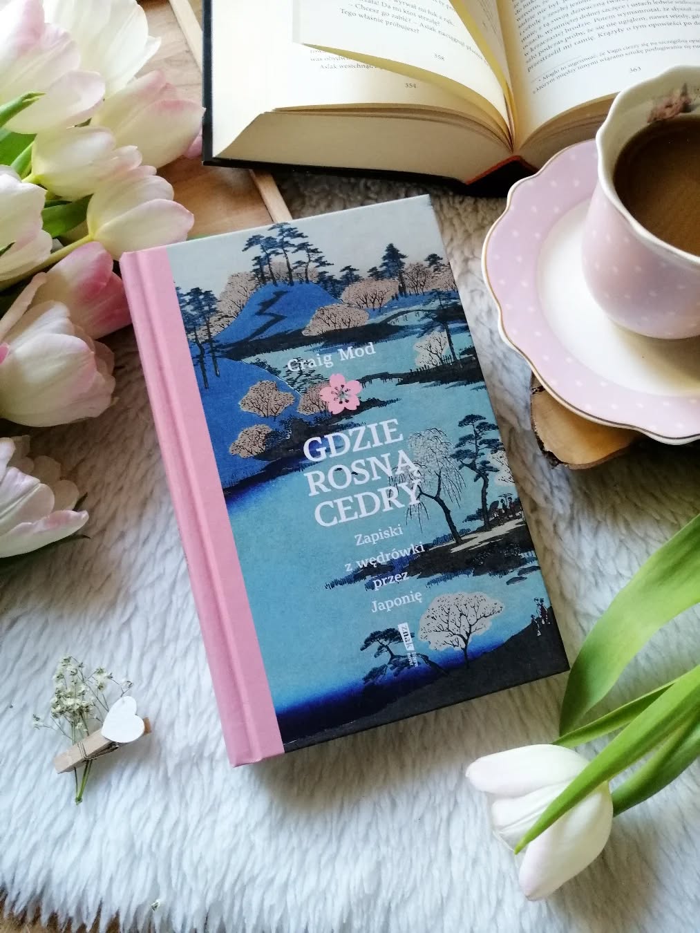 Dzień dobry 🤗  Książka, która skłania do zatrzymania się na chwilę.  “Gdy wędrujemy, towarzyszą nam ci, którzy szli przed nami. I ci, którzy nigdy nie podążą tym szlakiem".  “Gdzie rosną cedry. Zapiski z wędrówki przez Japonię” Craig Mod  Opowieść o Japonii, którą można czytać jak bardzo osobisty, nieoczywisty przewodnik. Z jednej strony jest to reportaż o miejscu, które zachwyca i przyciąga swoją odmiennością, z drugiej – zapis duchowej drogi, która skłania do refleksji. W tej historii odnajdziemy zarówno opowieść o kraju i jego historii, jak i motyw pielgrzymki – poszukiwania ciszy, równowagi i spokoju. To także bardzo intymna podróż, w której autor niesie na barkach ciężar żałoby.  Wędrówka staje się tu symbolem czegoś znacznie głębszego – jest próbą zajrzenia w głąb siebie. To rozważania o stracie, tęsknocie i relacjach, które zostawiają w sercu trwały ślad. Autor wraca myślami do przyjaciela z młodości, Bryana, którego już nie ma. Wspomnienia o nim towarzyszą mu w każdym kroku tej drogi.  Jest w tej książce coś niezwykle poruszającego. Tu wszystko opiera się na prostocie – na prawdziwych emocjach, zachwycie nad naturą, ale też na bólu, który niesie życie. To niespieszna, niemal medytacyjna podróż przez myśli i wspomnienia, przez stratę, która wciąż boli. Autor pozwala sobie na refleksję nad życiem, nad przemijaniem i nad przyjaźnią, która mimo śmierci wciąż trwa w pamięci. W ciszy natury próbuje odnaleźć ukojenie, którego tak bardzo potrzebuje.  Książkę wzbogacają czarno-białe fotografie, które pięknie dopełniają opowieść i pobudzają wyobraźnię. To obraz Japonii daleki od turystycznych pocztówek i katalogowych widoków.  Najlepiej czytać tę historię powoli, w ciszy pozwolić sobie na spokojną, nieco melancholijną podróż.  Warto po nią sięgnąć, polecam.  współpraca barterowa - @znak_literanova  #gdzierosnącedry #kochamczytać #ksiazkaojaponii #dobraksiążka